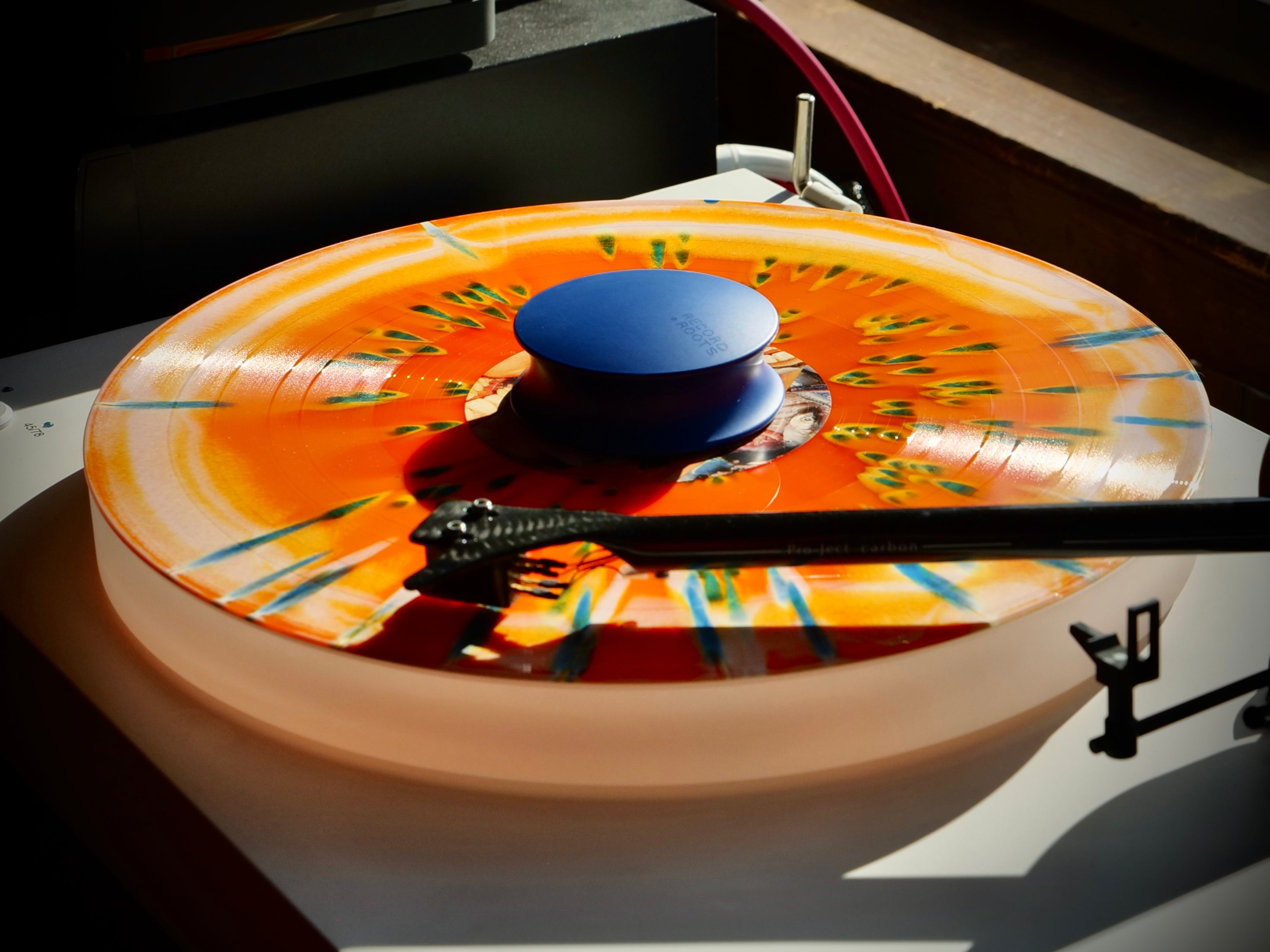 Blue Record Roots record weight on orange vinyl playing on a turntable